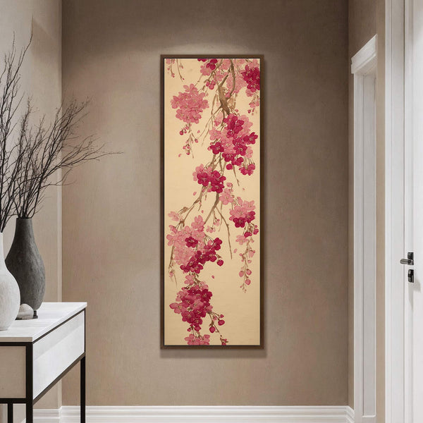 This vertical canvas wall art displays pink cherry blossoms on a tan background with a dark wood frame, hanging on a tan wall above a console table.