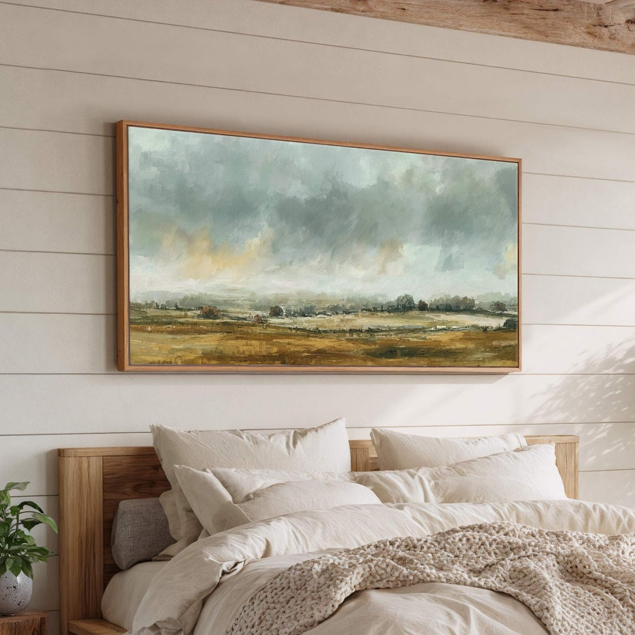 This horizontal, impressionistic canvas wall art depicts a muted landscape with a soft, earth-toned palette, framed by a natural wood floater frame, displayed above a bed with light linens on.