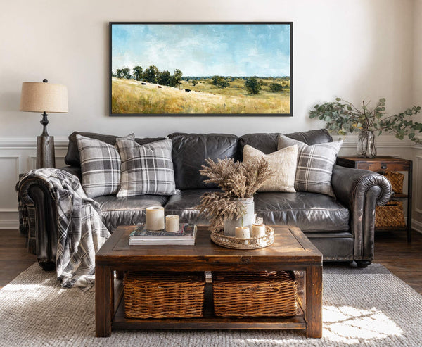 This horizontal canvas wall art features a pastoral landscape with a golden field under a bright blue sky, rendered in a textured impressionistic style. It hangs above a dark leather.