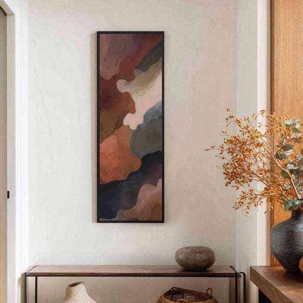 A vertical canvas print with an abstract design in warm earth tones is hung on a textured white wall above a dark wood console table with a vase and a.