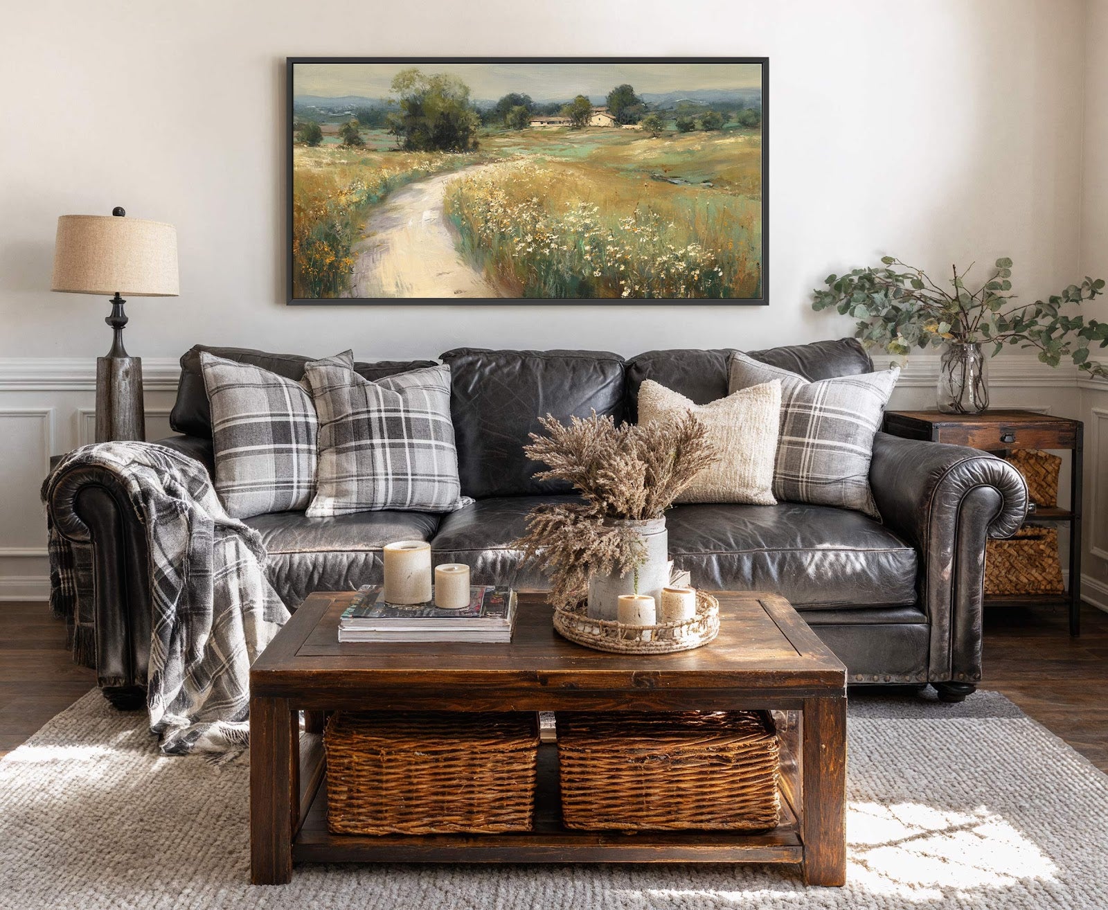 This horizontal canvas print features a rustic landscape painting with a muted, earthy color palette and an impressionistic style. It is displayed above a dark leather sofa on a light-colored.