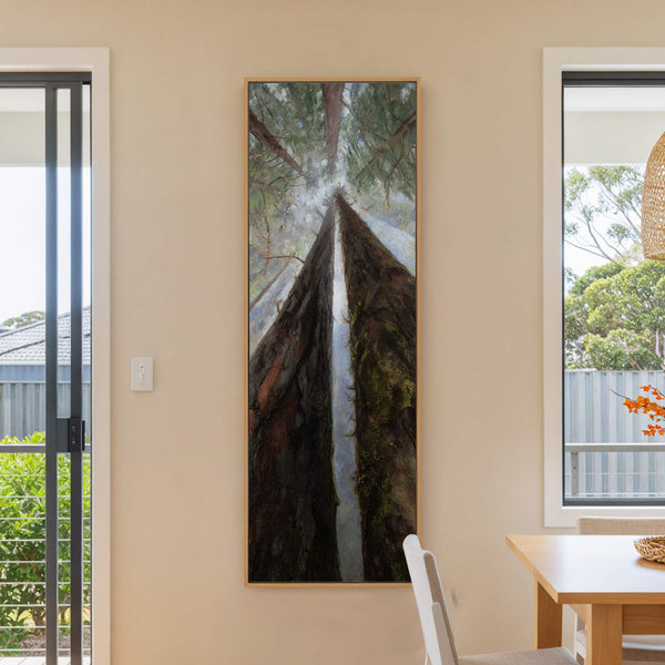 This vertical canvas print features a dramatic, impressionistic view looking up through towering redwood trees, rendered in dark greens and earthy browns, framed by a light wood floater frame. The.