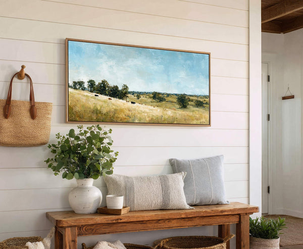 This horizontal canvas wall art depicts a pastoral landscape with cows grazing in a field under a bright blue sky, rendered in an impressionistic style with a warm, natural palette.