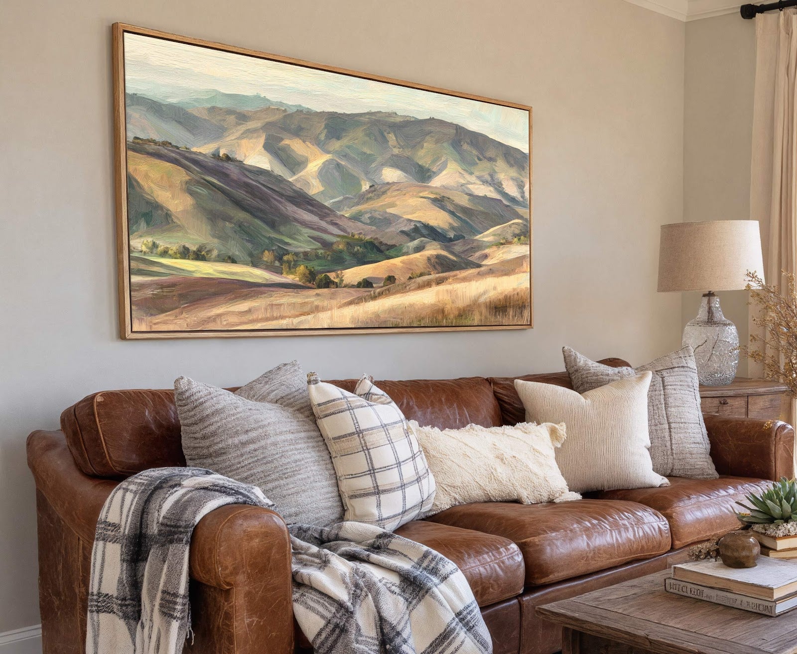 This horizontal canvas print features an impressionistic painting of rolling hills with a palette of greens, browns, and blues, set in a living room with a brown leather sofa and.