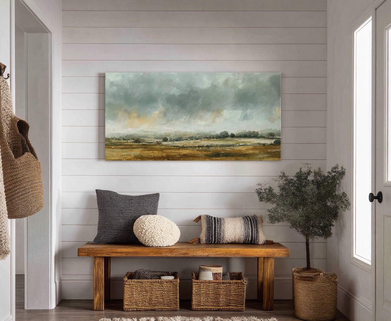 This horizontal canvas print features an impressionistic landscape with a muted palette of greens, browns, and grays, displayed above a wooden bench with woven baskets on white shiplap walls.