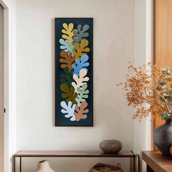 This vertical canvas print features abstract leaf shapes in a soft palette of blue, yellow, green, and brown against a dark background, displayed above a console table on a white.