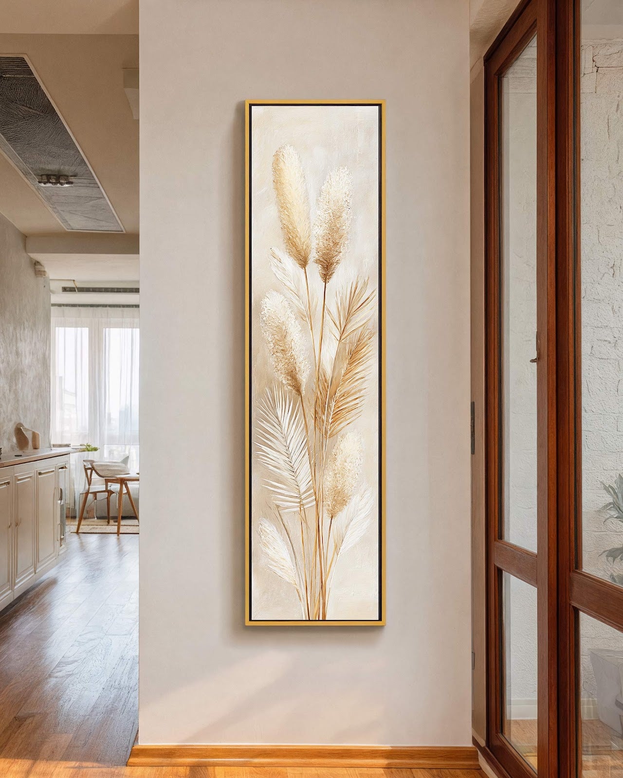 This vertical art print showcases textured pampas grass in cream and tan tones, presented in a gold floater frame on an off-white hallway wall next to a wooden door.