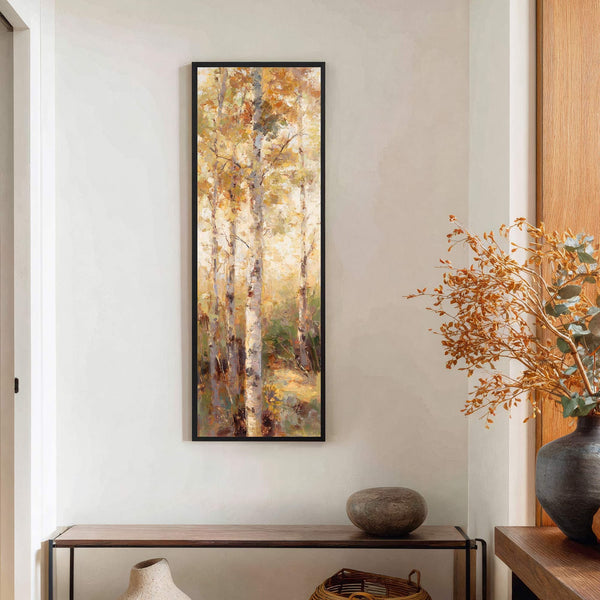 A vertical canvas print features an impressionistic forest scene with birch trees and a warm, golden palette, framed in black and hung on a white wall above a wooden console.