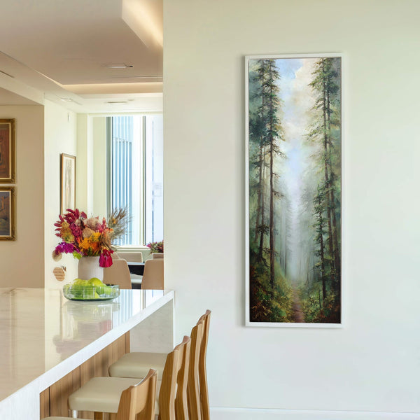 This vertical, realist oil painting print depicts a misty forest path with tall pine trees in rich greens and browns, framed in white and displayed on a cream wall in.