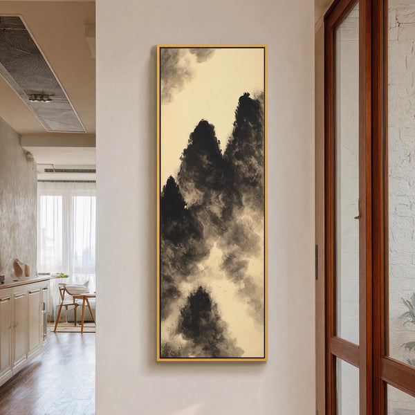 This vertical canvas wall art displays monochromatic ink-wash mountain peaks in black and cream, hanging in a gold floater frame on a white hallway wall near a wooden glass door.