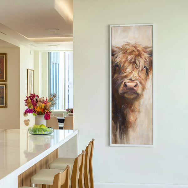 This vertical canvas wall art features a fluffy Highland cow in a warm, neutral palette and Impressionist style, framed in white, displayed on a cream wall next to a vase.