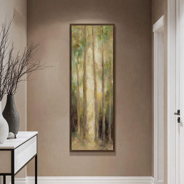 This vertical, abstract forest painting print in earthy greens and yellows is set against a taupe wall, with a console table and vase visible in the foreground.
