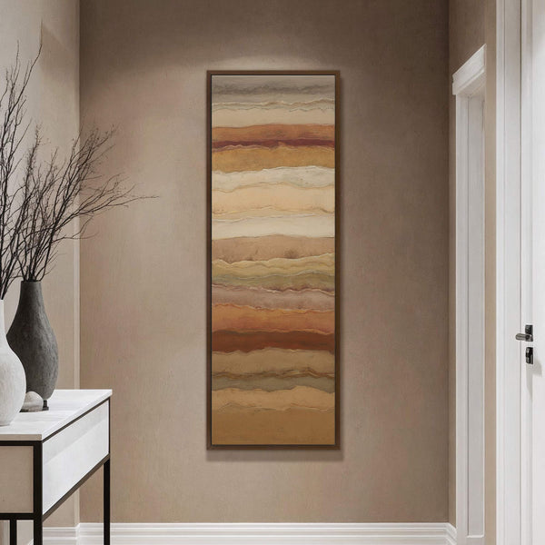 This vertical abstract painting print features horizontal bands in earthy tones like rust, beige, and green, framed in natural wood. It is displayed in a hallway with beige walls and.