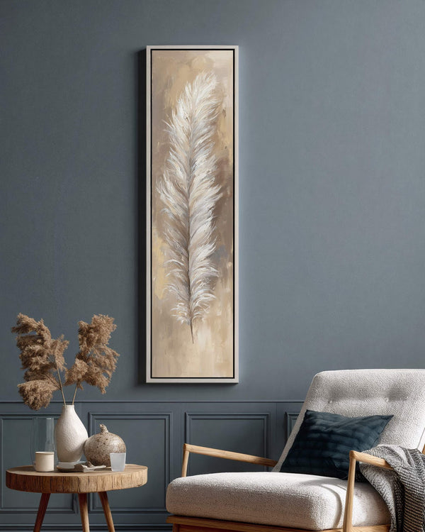This vertical canvas print features a textured white feather in neutral tones, displayed in a white floater frame on a blue paneled living room wall beside a white armchair.