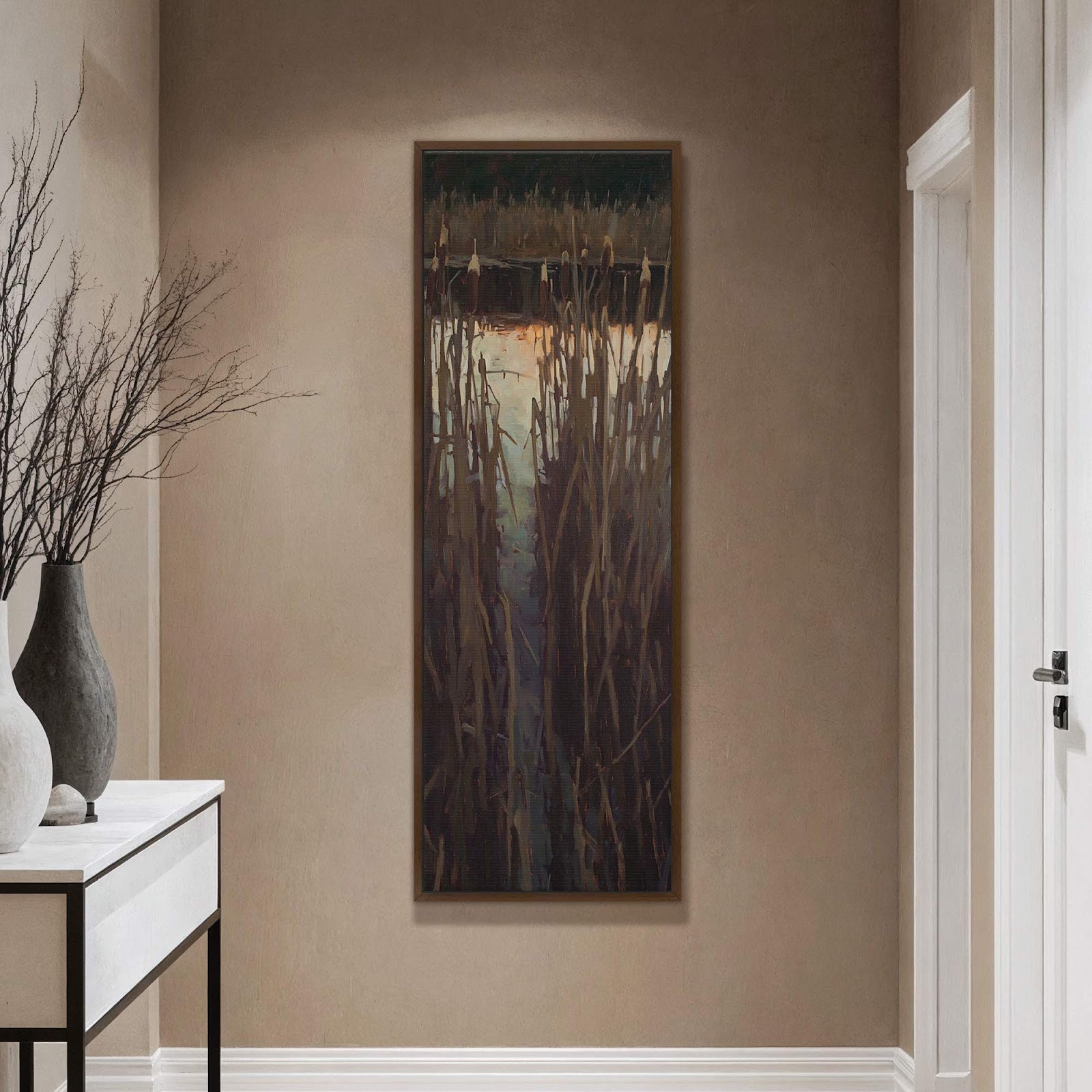 This vertical canvas wall art print displays a painterly depiction of cattails by a body of water, featuring a muted palette and impressionistic style, framed in brown on a taupe.