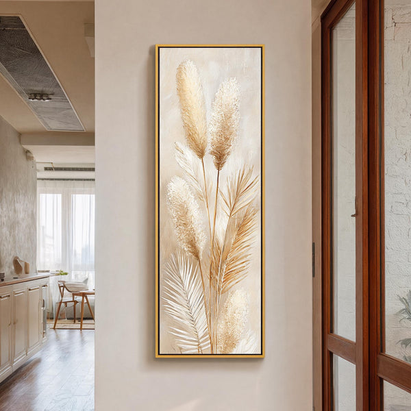 This vertical botanical art print features textured pampas grass in beige tones, presented in a gold floater frame on a neutral hallway wall next to a wooden glass door.
