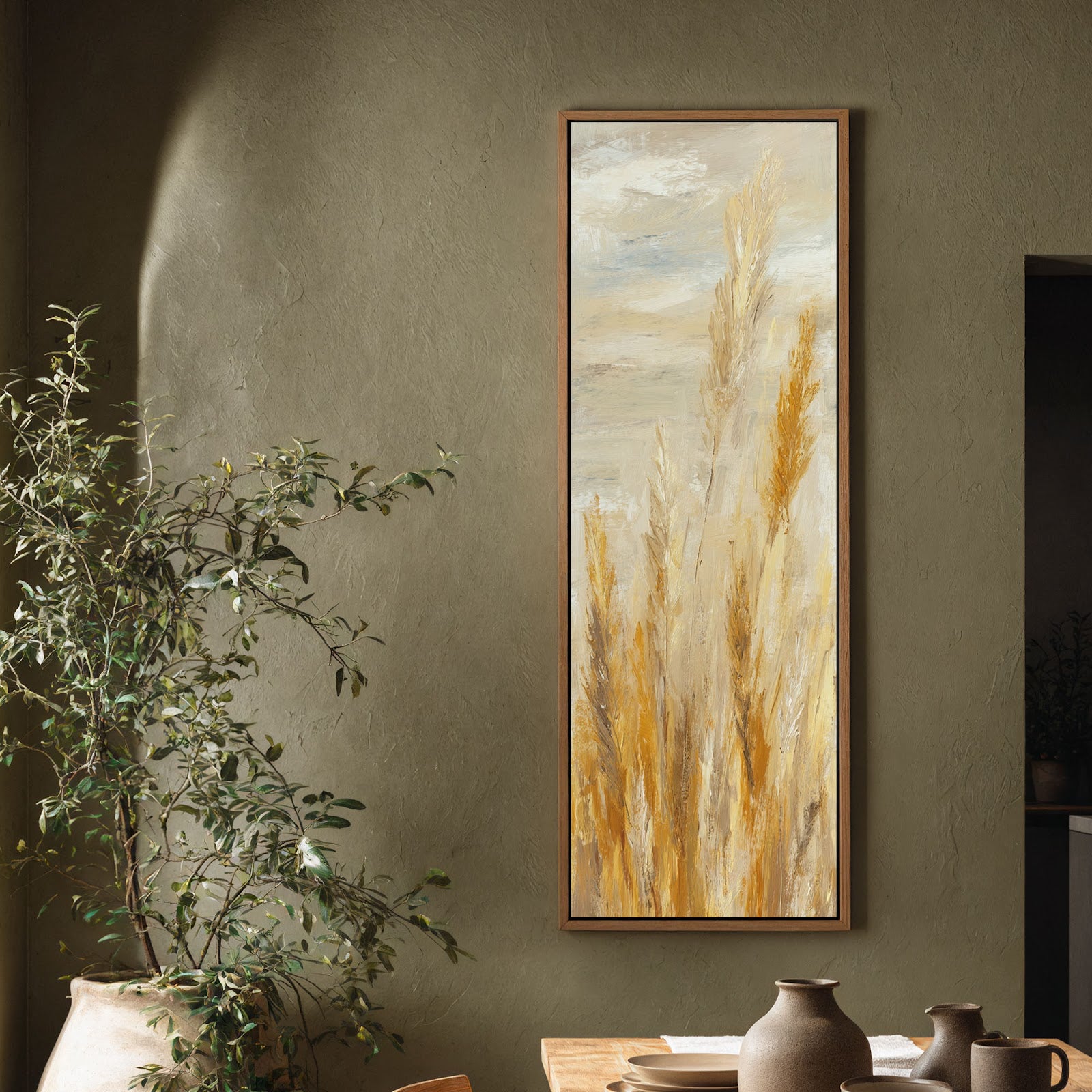 This vertical painterly art print features abstract ochre reeds in an oak floater frame, hung in a dining area with textured olive walls beside a large potted plant.