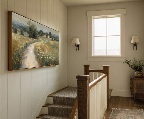 This horizontal canvas wall art depicts a landscape with a dirt path winding through grassy fields and trees, using a muted green and yellow palette. It is displayed in a.