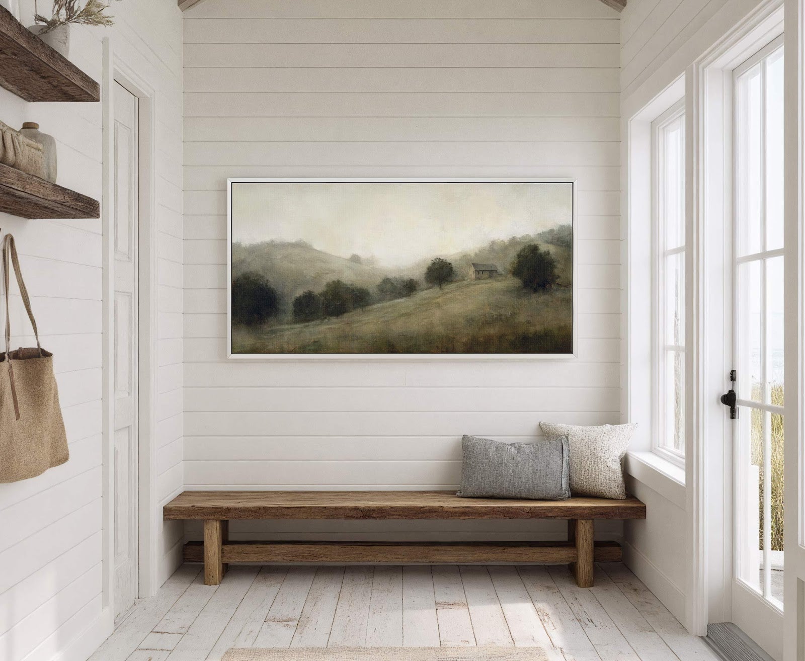 This horizontal canvas wall art print displays a misty landscape with a small building, using a muted green and brown palette in a painterly style, hung on a white paneled.