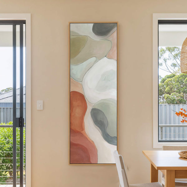 This abstract canvas wall art features a fluid organic design in a muted palette of terracotta, sage green, and cream, framed in natural wood and displayed on a neutral wall.