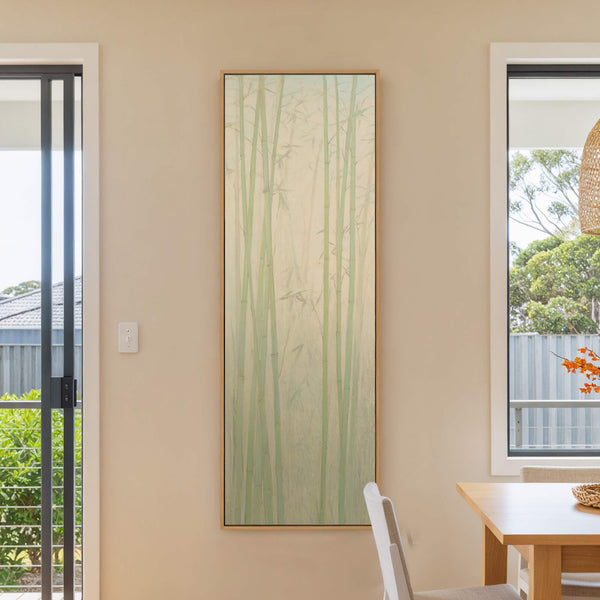 This vertical canvas wall art features a serene bamboo forest rendered in a pale green and cream palette with a minimalist style, displayed on a beige wall next to a.