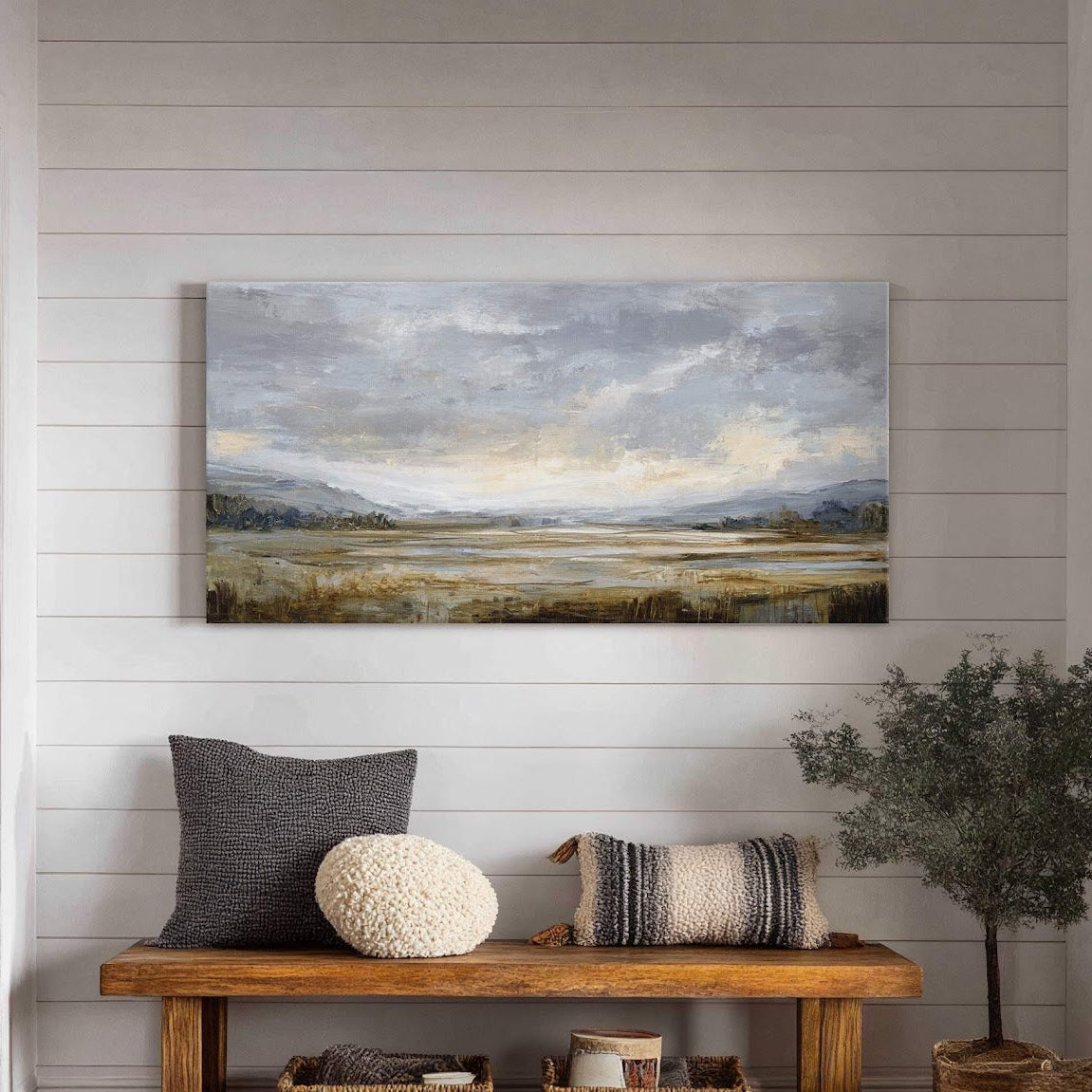 This horizontal canvas print showcases an impressionistic landscape in a muted palette of grays, blues, and earthy tones, hanging above a wooden bench with decorative pillows and baskets in a.
