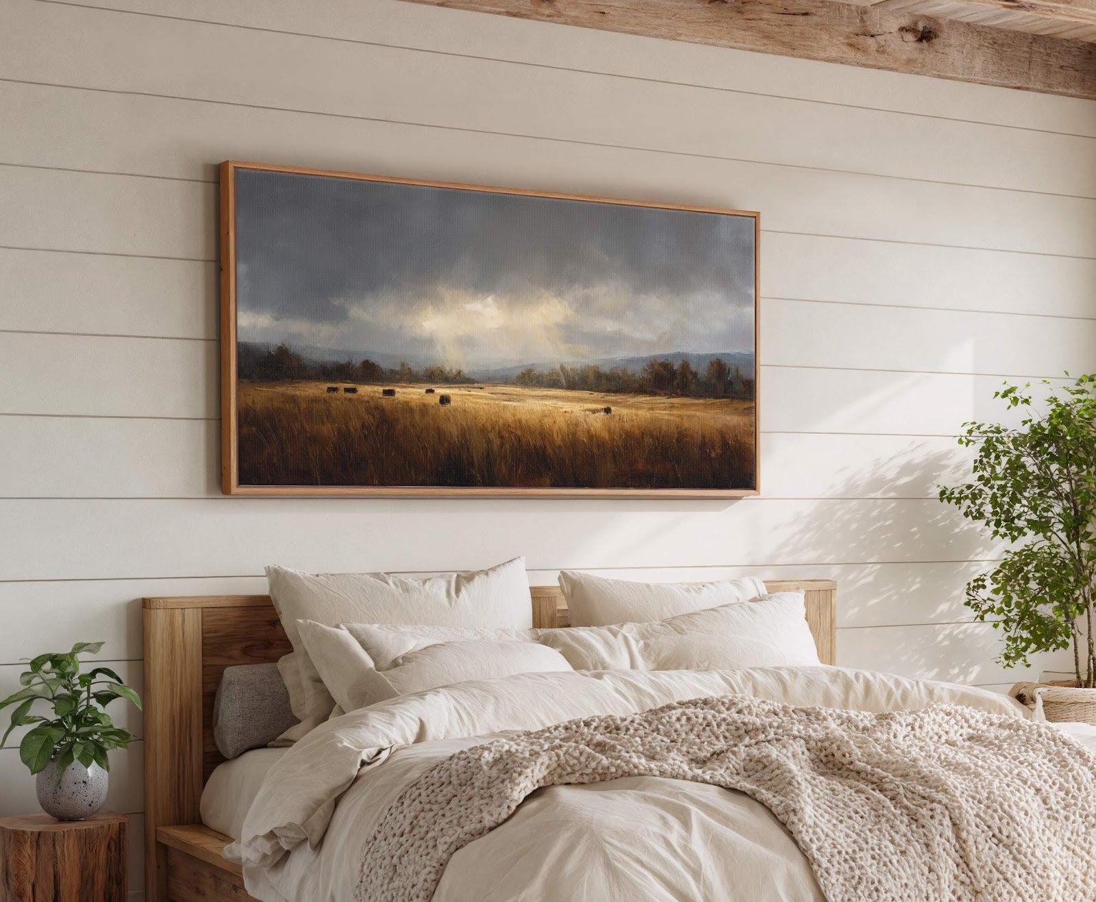This horizontal canvas print features a dramatic landscape with hay bales in a field under a stormy sky with golden light breaking through, framed in natural wood and hung above.
