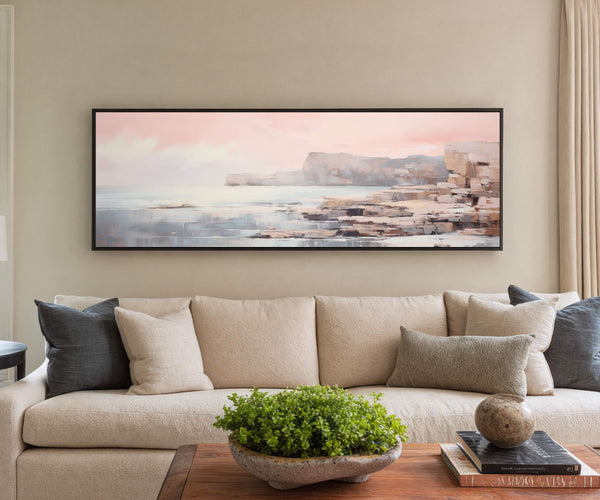 Framed seascape canvas wall art with coastal cliffs and pastel sky displayed above a beige sofa in a modern living room interior
