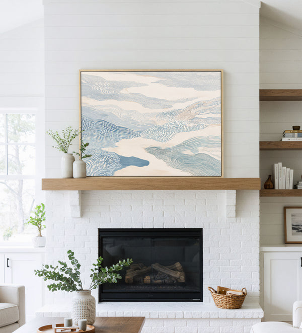 Natural framed abstract art print featuring layered, flowing shapes with fine textured lines in muted blues, creams, and beiges, resembling clouds or currents, displayed above a white fireplace mantel in a bright, modern living room