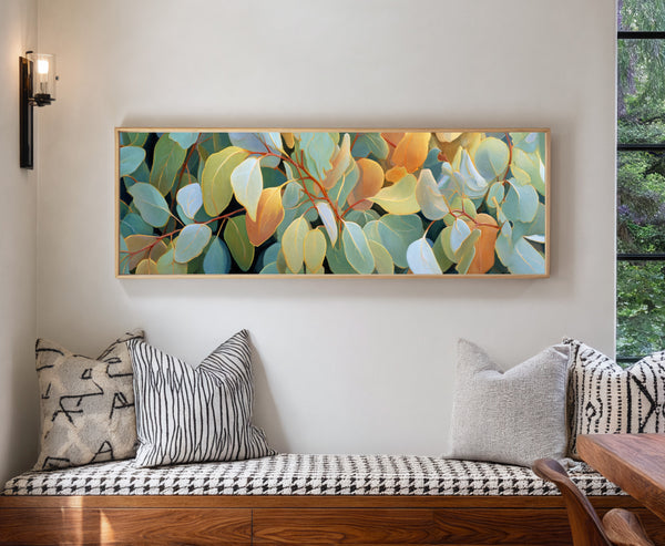 Framed eucalyptus leaf canvas wall art displayed above a modern bench with patterned cushions in a bright, contemporary interior.