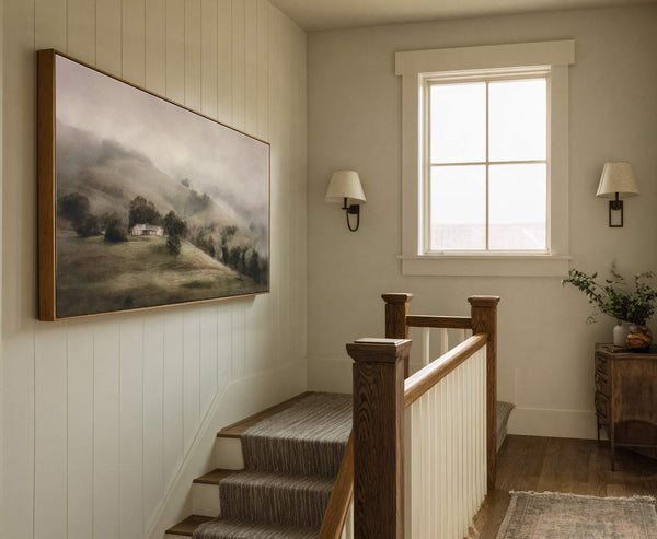This horizontal canvas wall art showcases a foggy landscape with a white house and trees, utilizing a muted green and gray palette in a painterly style, displayed above a staircase.