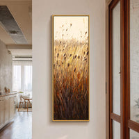 This vertical canvas wall art showcases a modern impressionist painting of reeds with a warm, golden palette, displayed on a light-colored wall next to a wooden door frame.