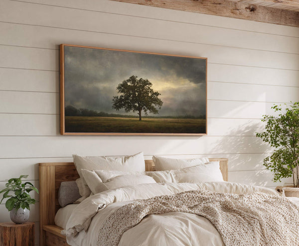 This horizontal landscape canvas print features a solitary oak tree in a field under a dramatic, cloudy sky with a sliver of yellow light breaking through. The artwork is framed.