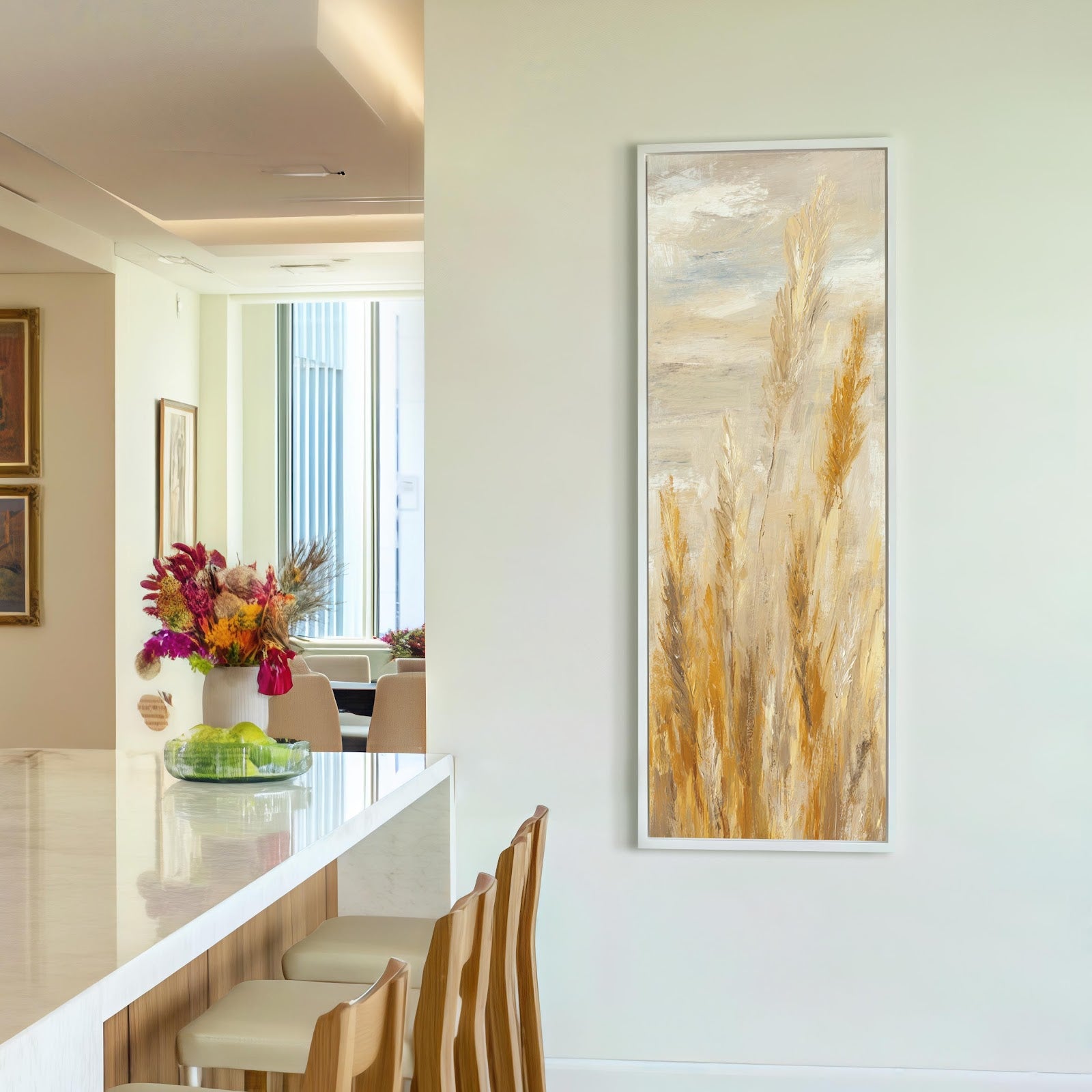 This vertical canvas wall art depicts abstract golden pampas grass in an ochre palette, displayed in a white floater frame on a white kitchen wall near a breakfast bar.