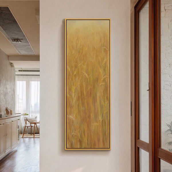 This vertical canvas print features an impressionistic artwork of golden wheat stalks in warm tones, framed with a thin gold floater frame, displayed on a neutral wall in-room wall next.