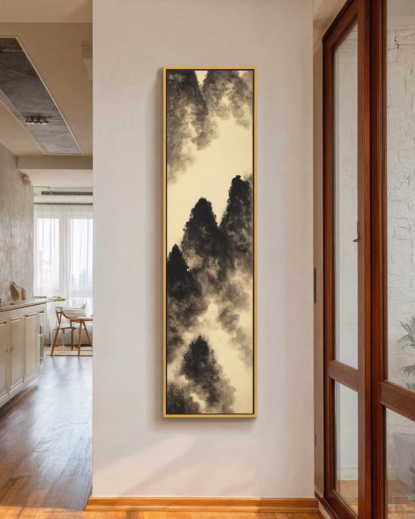 This vertical canvas print of monochromatic ink-wash mountains on a beige background is displayed in a gold floater frame on a white hallway wall beside a wooden door frame.