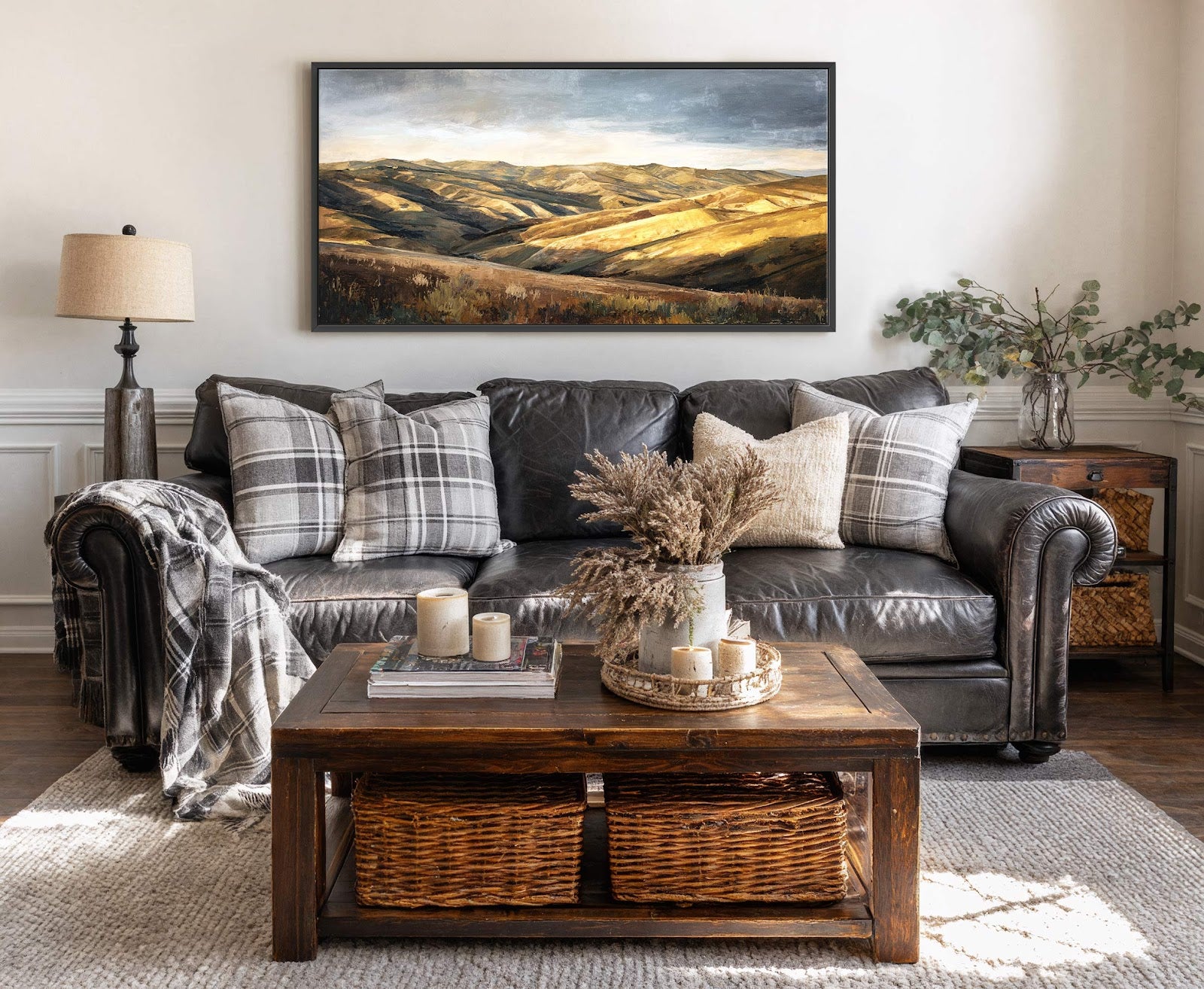 This horizontal canvas wall art print features a landscape painting with a warm, golden palette in a realist style, displayed above a dark leather sofa in a living room with.