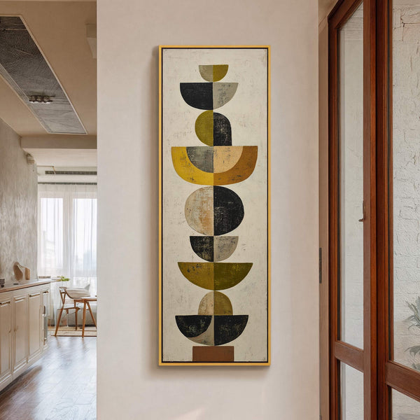This vertical canvas wall art features a mid-century modern abstract composition in a palette of mustard yellow, olive green, black, and gray. It is framed in gold and hangs on.