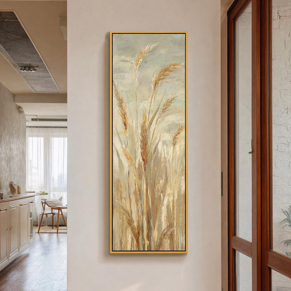 This vertical canvas wall art features impressionistic wheat stalks in a neutral palette, showcased in a gold floater frame on a white hallway wall near a wooden glass door.