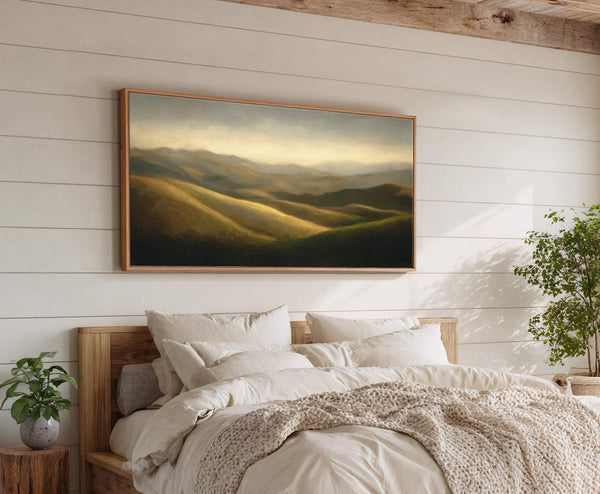 This horizontal canvas wall art depicts rolling hills in muted earth tones and soft light, framed with a natural wood floater frame, displayed above a bed with cozy neutral bedding.