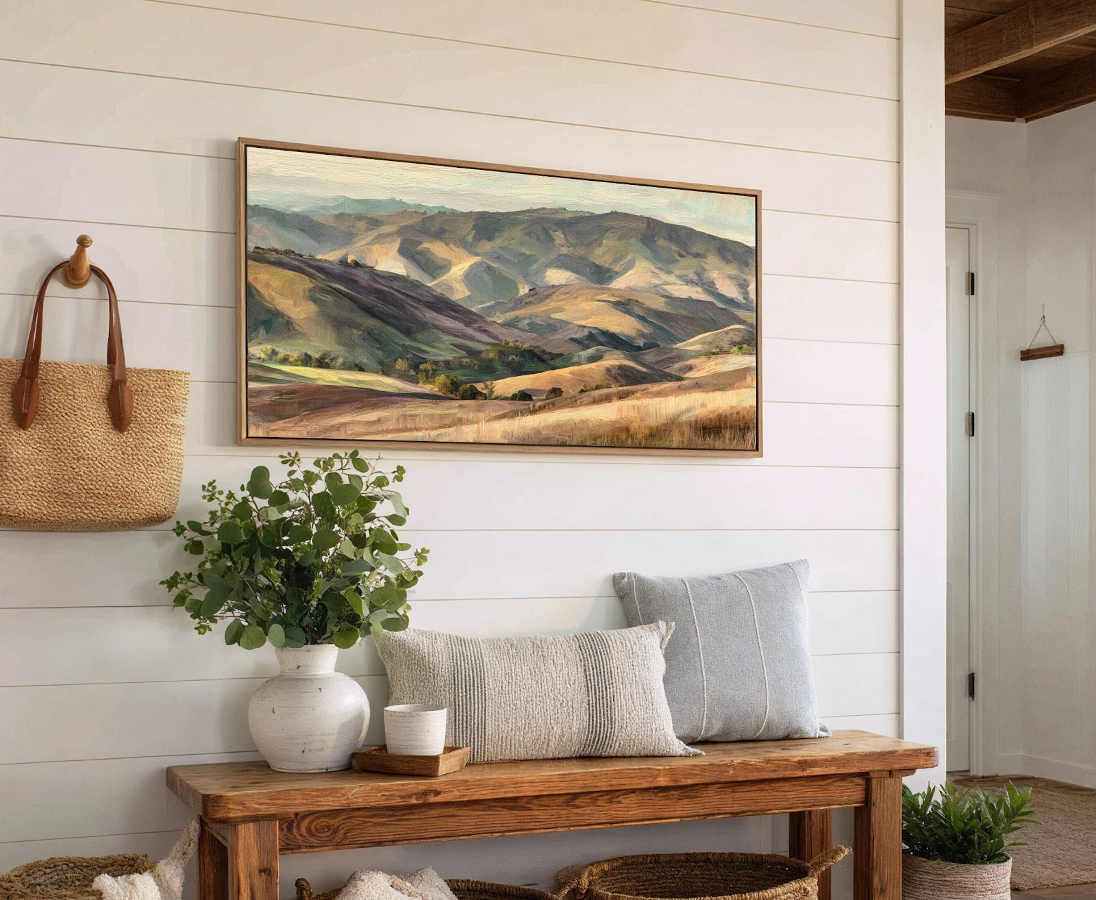 This horizontal canvas wall art depicts rolling hills with a palette of greens, browns, and blues in a painterly style, displayed in a room with white shiplap walls above a.