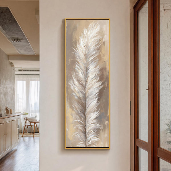 This vertical canvas wall art features an impressionistic white feather in a neutral palette, displayed in a gold floater frame on a cream hallway wall near a window.