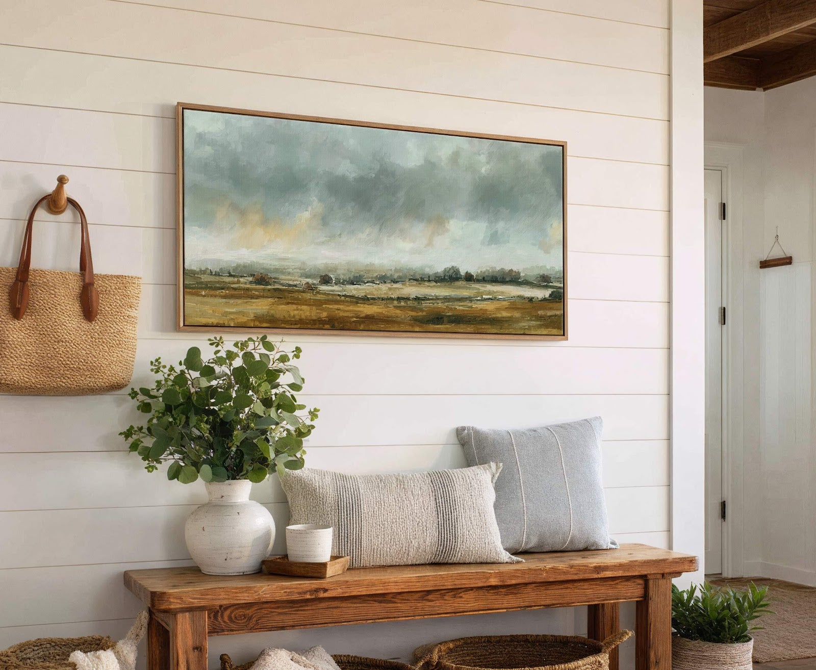This horizontal canvas wall art features a muted, impressionistic landscape with a palette of blues, greens, and earthy browns, framed in natural wood and displayed above a rustic wooden bench.