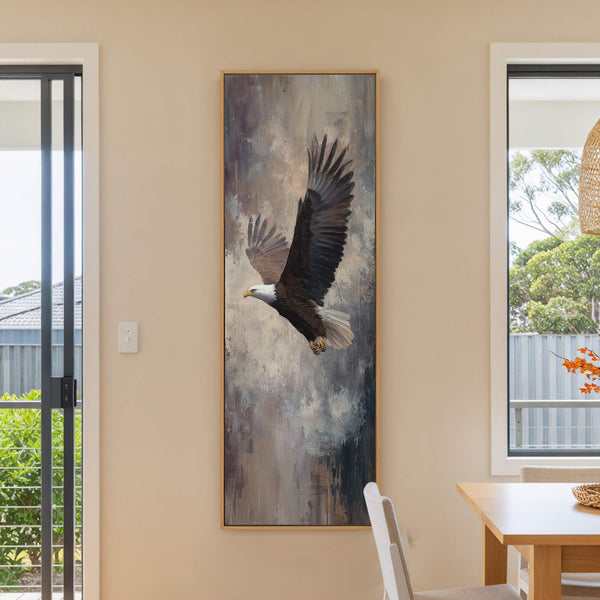 This vertical canvas wall art depicts an eagle in flight against a textured, abstract background in muted earthy tones, framed in a natural wood finish and displayed on a light.