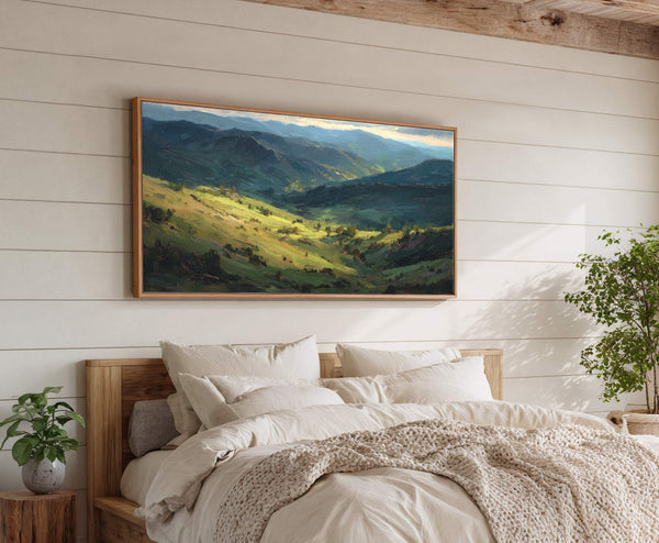 This landscape painting print features a vibrant green valley and distant mountains in a painterly style with a natural wood floater frame, displayed above a bed with a wooden headboard.