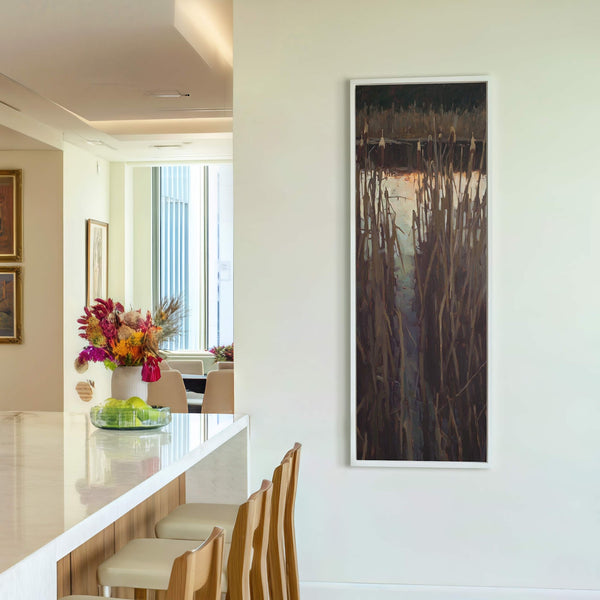 This vertical canvas wall art displays a dark, moody landscape with reeds in a painterly style and a palette of browns and grays, framed in white and hanging on a.