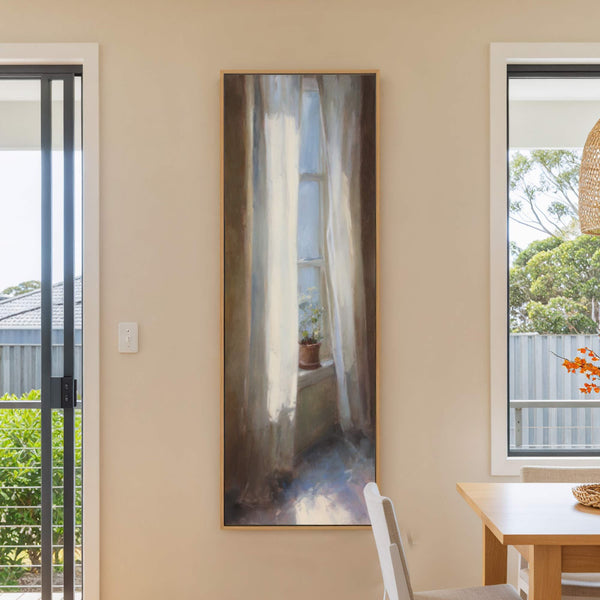 This vertical, oil painting print features a potted plant visible through sheer curtains in a soft, impressionistic style with a muted palette. It is framed in natural wood and hangs.