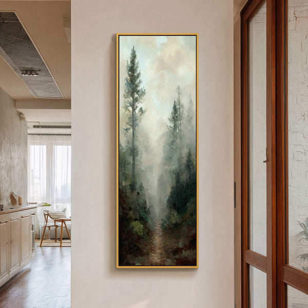 This vertical, gold-framed canvas wall art depicts a misty forest path with dark green trees and a muted palette, hanging on a light-colored wall near a wooden door.