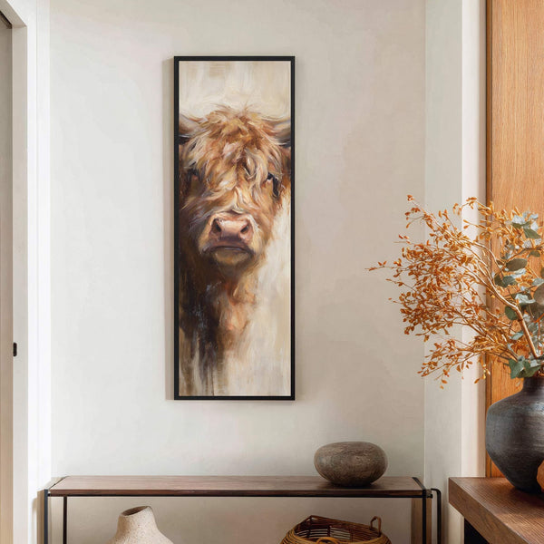 This vertical, impressionistic art print features the front view of a fluffy Highland cow with a warm brown and cream palette, hanging on a white wall above a slim console.