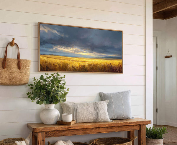 This horizontal canvas print captures a dramatic landscape of golden fields under a dark, cloudy sky with bursts of sunlight, rendered in a painterly style. It is displayed on a.